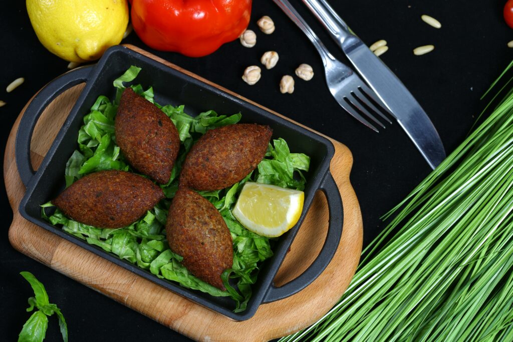 Tasty kibbeh served with fresh vegetables, a lemon wedge, and herbs in a flatlay food composition.