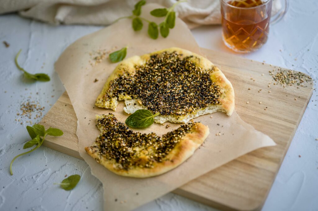 Delicious traditional Manakish topped with zaatar served on a wooden board with tea.